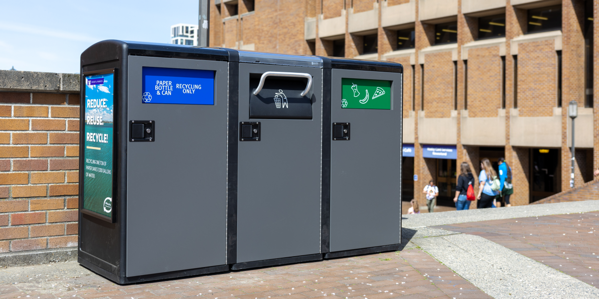 waste bins outside that have three flaps; one says paper, bottle and can recycling only, another has a garbage can and the third has food items on it 