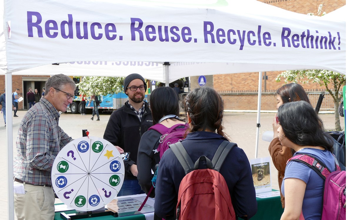 two people talking to other people under a tent that read reduce. reuse. recycle. rethink.