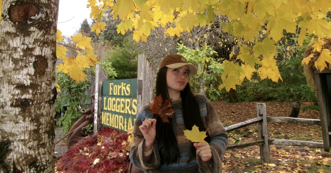 Brianna in a forest with all the tree leaves a bright Fall yellow