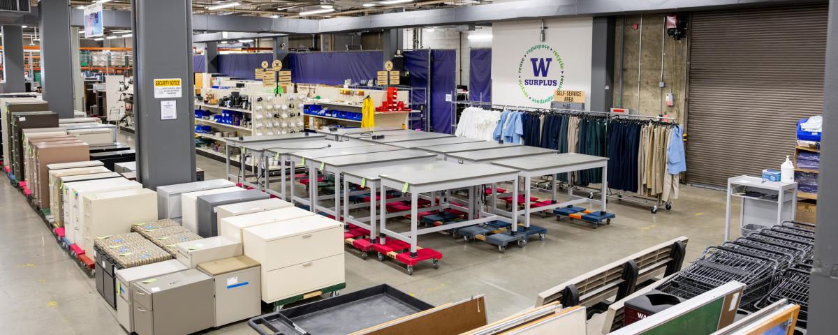 warehouse containing filing cabinets, desks and other items with a logo on a wall saying W Surplus