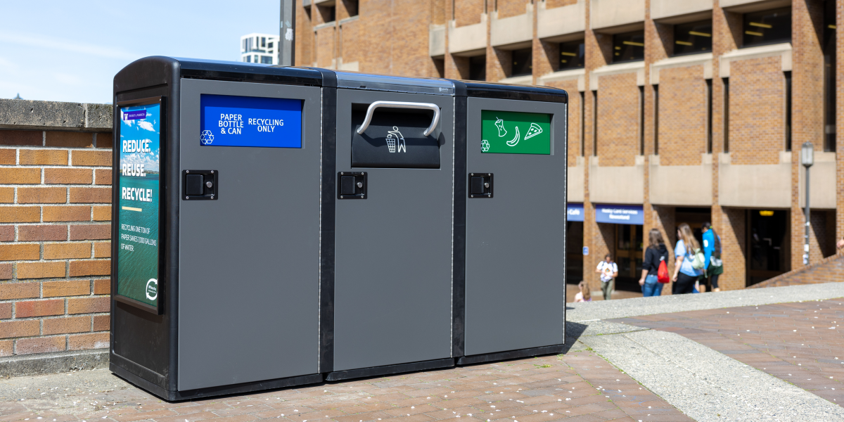 waste bins outside that have three flaps; one says paper, bottle and can recycling only, another has a garbage can and the third has food items on it