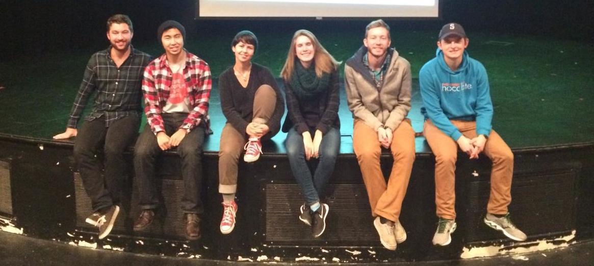 Members of the Green Husky Coalition sit at the edge of a stage.