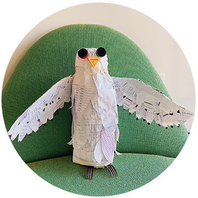a bird sculpture made out of scantrons sitting on a green chair