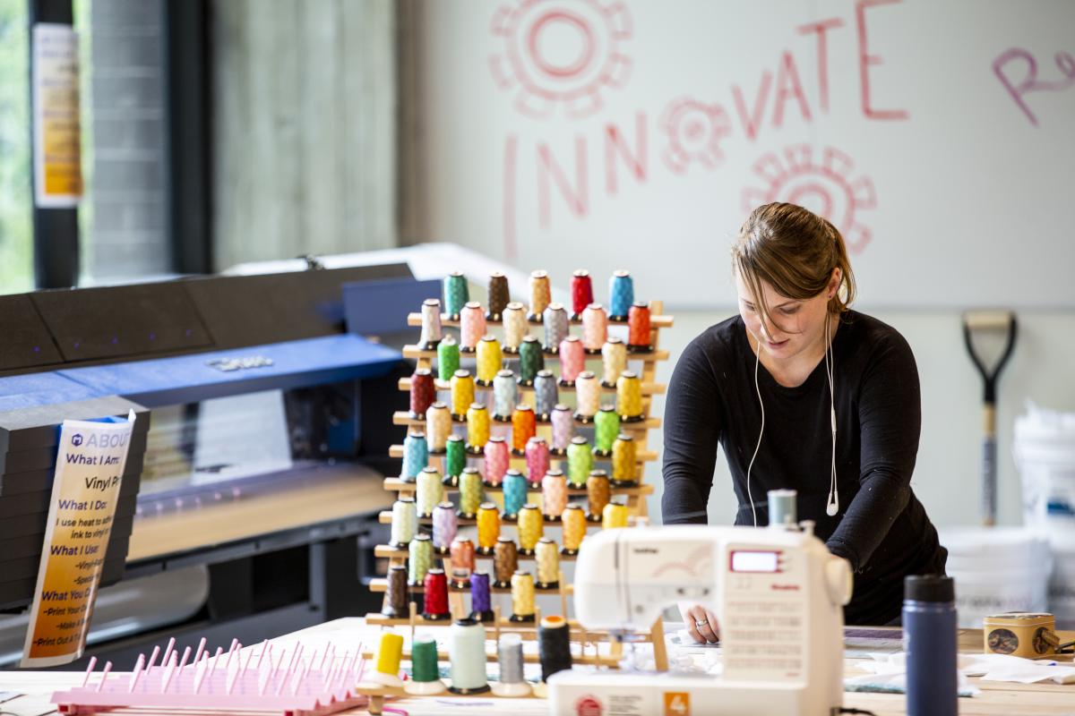 person behind a sewing machine and various spools of colored sewing threads