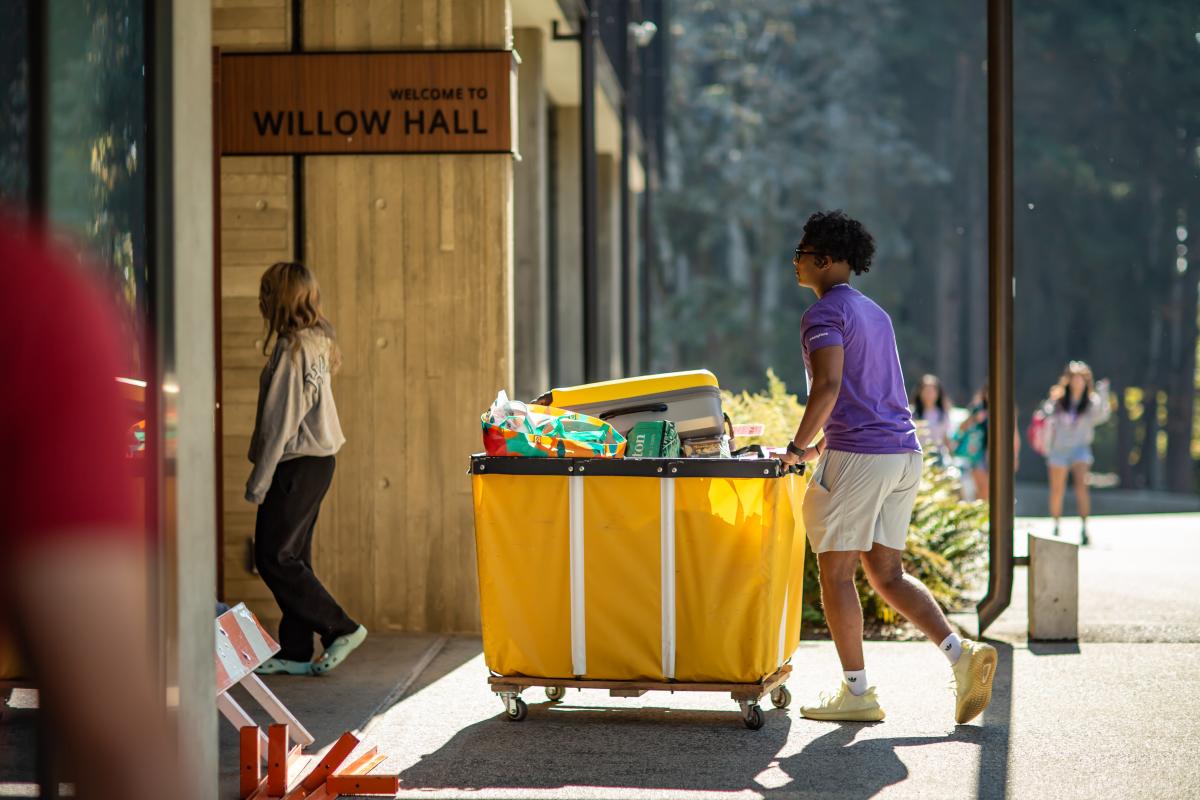 students moving into a residence hall with luggage in a cart