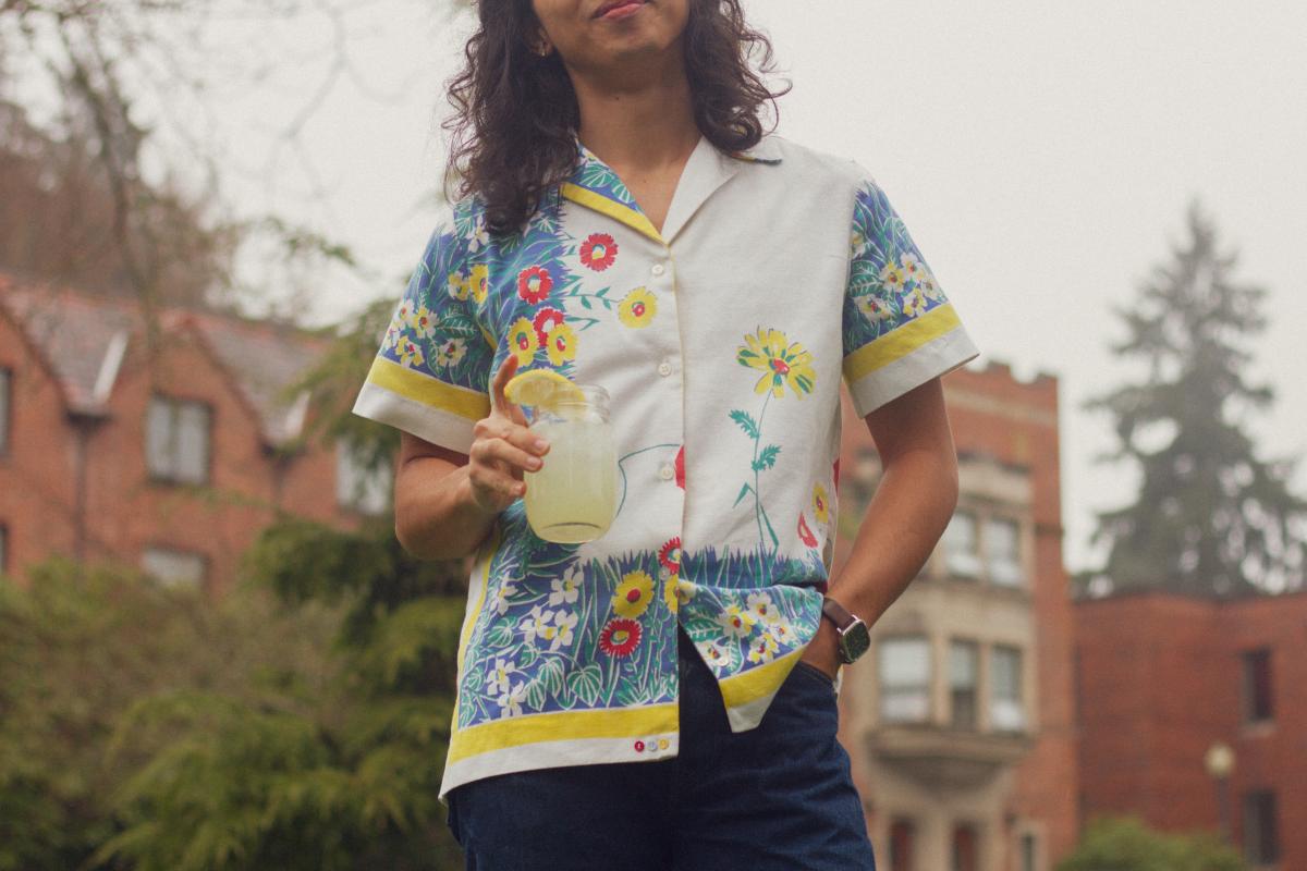 person with longer hair wearing a handmade shirt and holding a mason jar of lemonade
