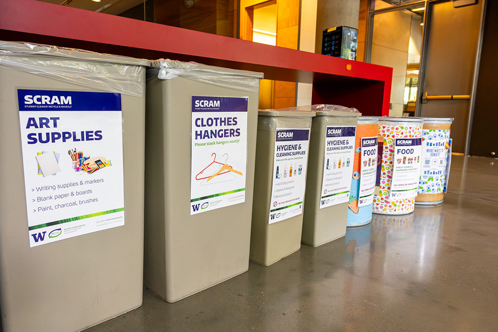 seven bins of various sizes with signs on them that say "scram" and types of donations