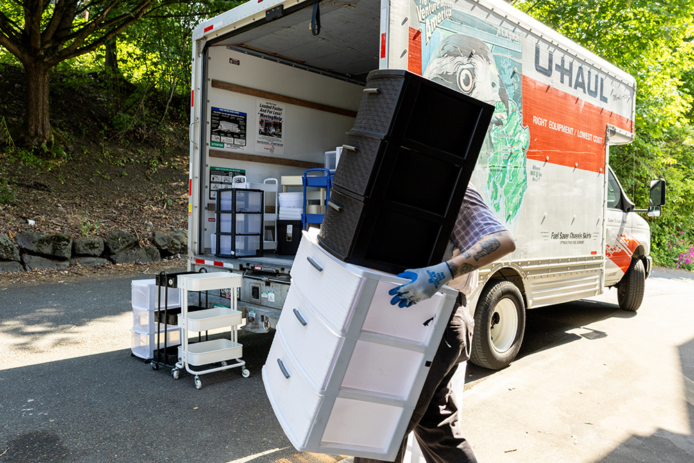 person loading two plastic storage drawers into a U-Haul truck. Other storage organizers can be seen in the U-Haul truck as well.