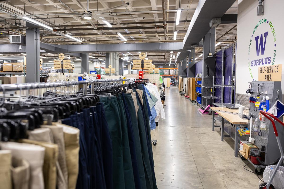 a rack of cloths with other items behind; a wall that says uw surplus on the right