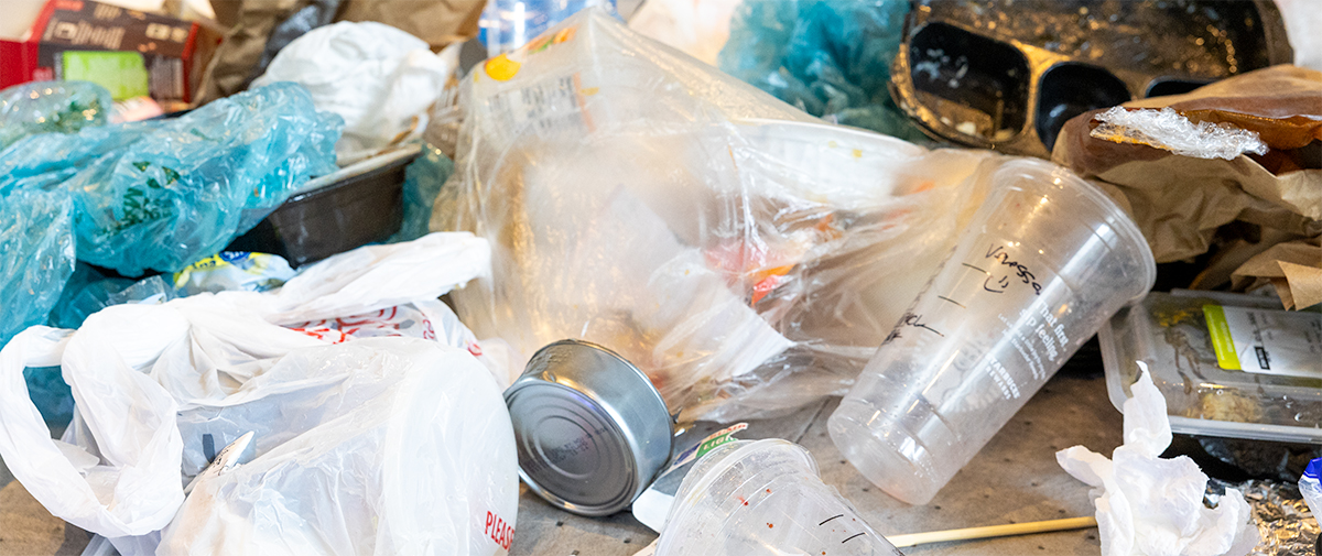 a pile of various items including plastic bags, an aluminum can, dirty containers, and an empty Starbucks cup,