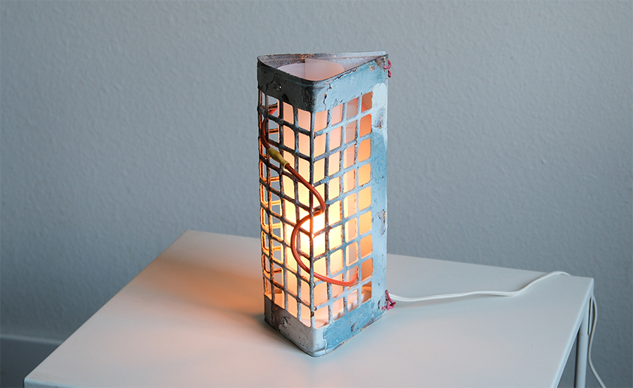 a lit lamp constructed of derelict metal grate material with a red wire interspersed within the openings