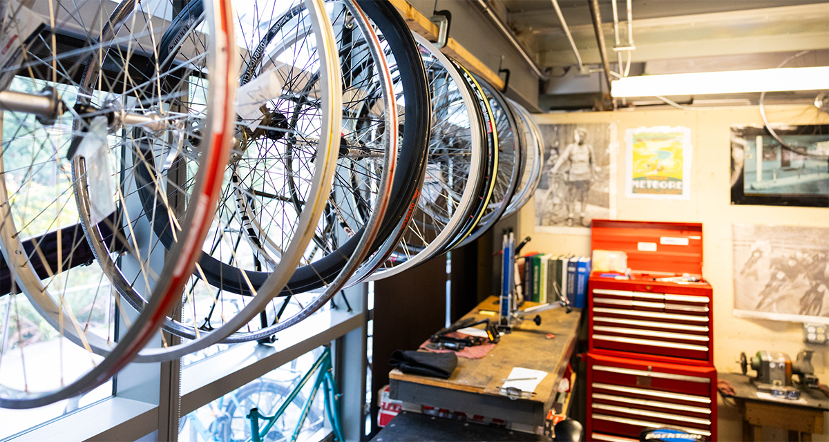 bike wheels hanging on a left wall with windows, on the right is a wall with a toolbox and posters