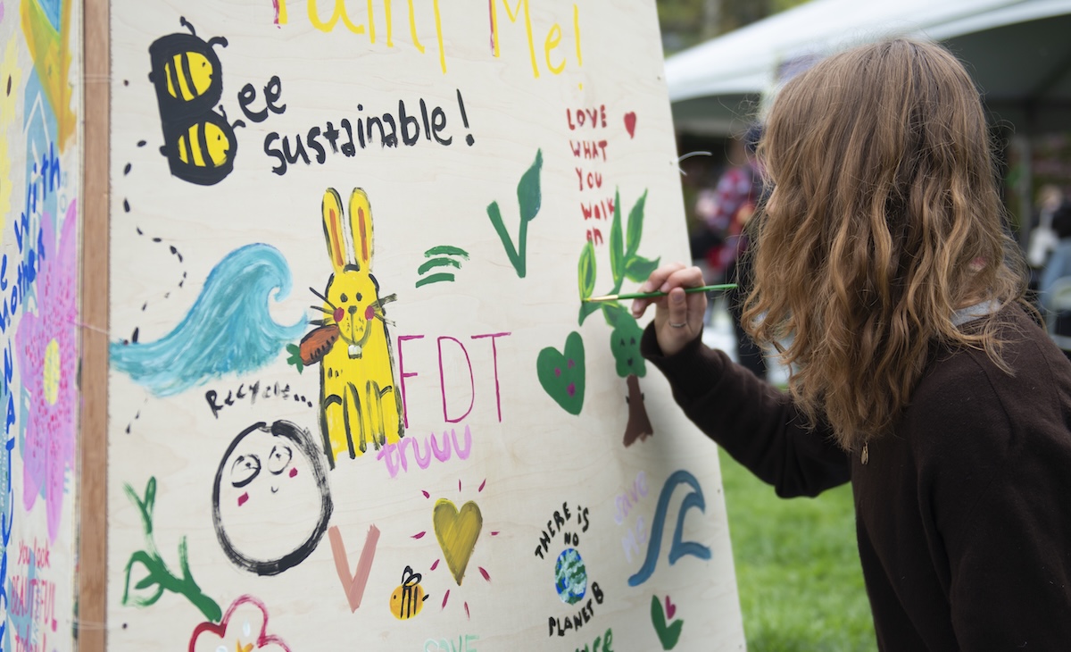 student painting a large canvas that lots of different people have added sustainability images to