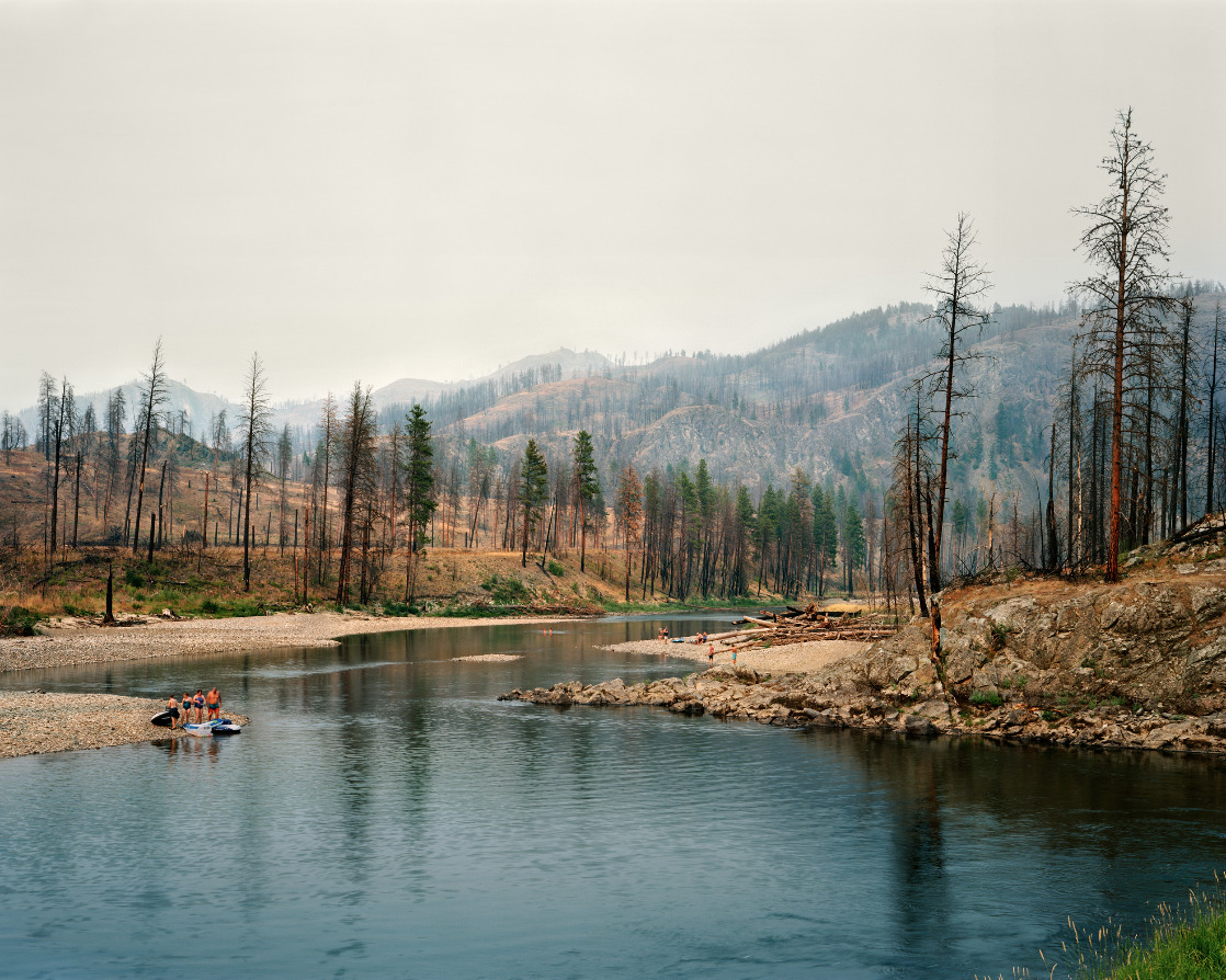 view of a river in the mountains surrounded by burned trees from a wildfire