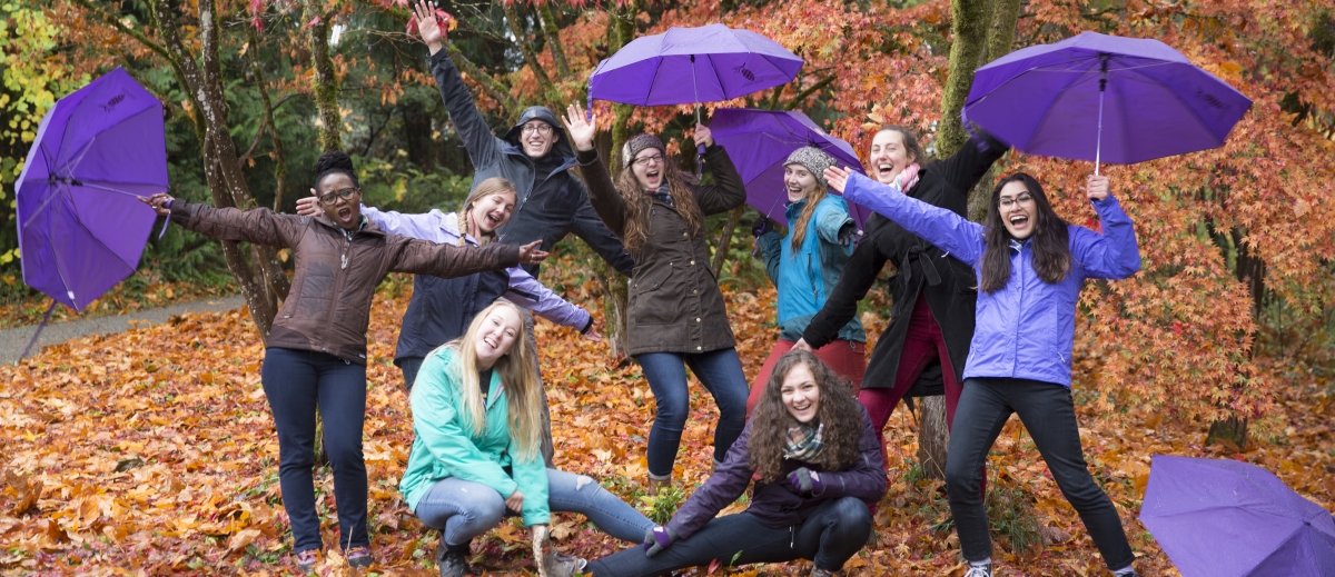 Students in forested area posing with purple umbrellas